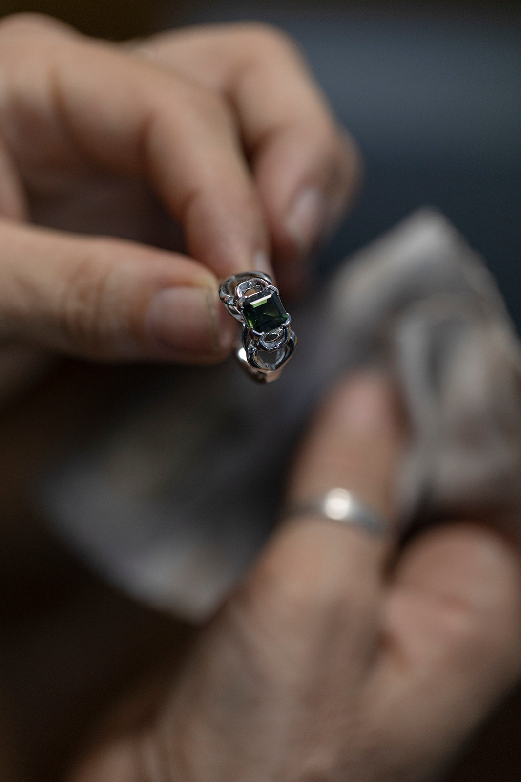 A pair of hands hold a white gold and green parti sapphire ring with soft focus on the hands and the ring in focus
